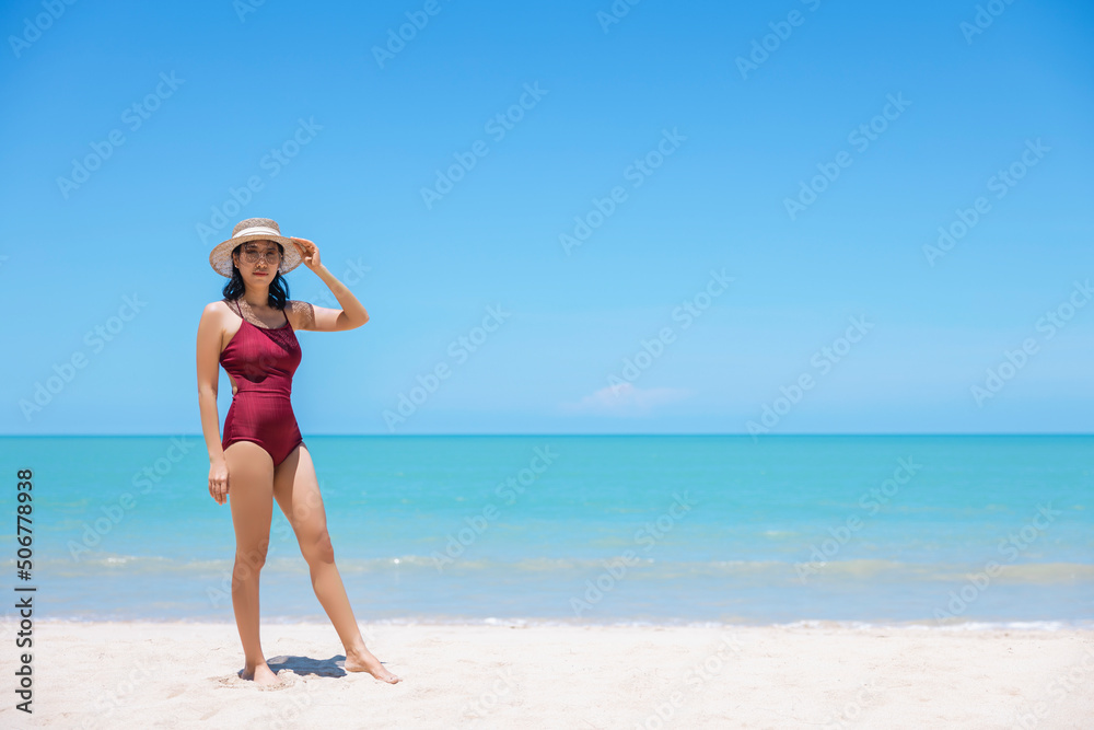 Young women in bikini and straw hat stand on tropical beach enjoying looking view of beach ocean on hot summer day. Blue sea in background. Khao Lak, Phang Nga, Thailand. Summer vacation concept Young women in bikini and straw hat stand on tropical beach enjoying looking view of beach ocean on hot summer day. Blue sea in background. Khao Lak, Phang Nga, Thailand. Summer vacation concept