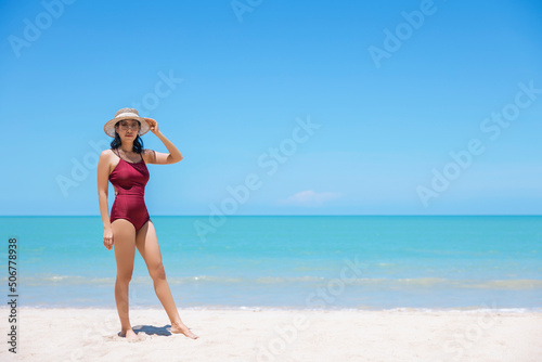 Young women in bikini and straw hat stand on tropical beach enjoying looking view of beach ocean on hot summer day. Blue sea in background. Khao Lak, Phang Nga, Thailand. Summer vacation concept