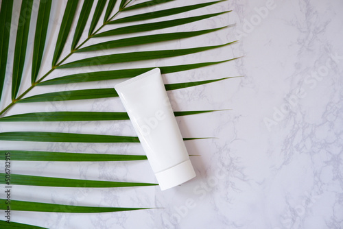A blank white squeeze bottle plastic tube with tropical palm leaf on White marble background. Packaging of cream, lotion, gel, facial foam or skincare. Cosmetic beauty product branding mock-up.  photo