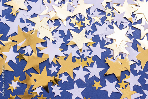 Golden stars and white confetty on blue background, selective focus. Festive holiday pastel backdrop.