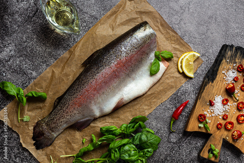Raw trout fish on parchment. Next to lemon, spices and herbs for cooking.