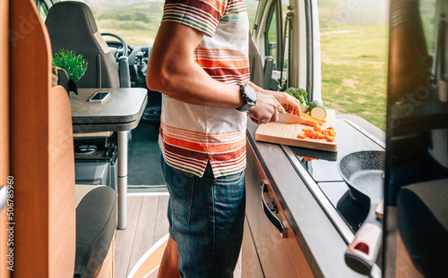 Unrecognizable young man cooking vegetables in a camper van