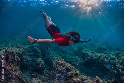 Girl diving holding the breath with rays of sun entering the water in the background