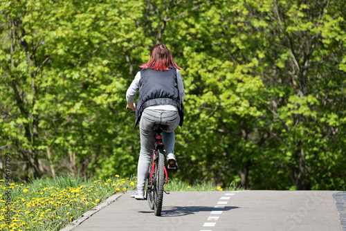 Wallpaper Mural Girl in jeans with red dyed hair riding on a bicycle in a green park. Woman cyclist, spring or summer leisure Torontodigital.ca