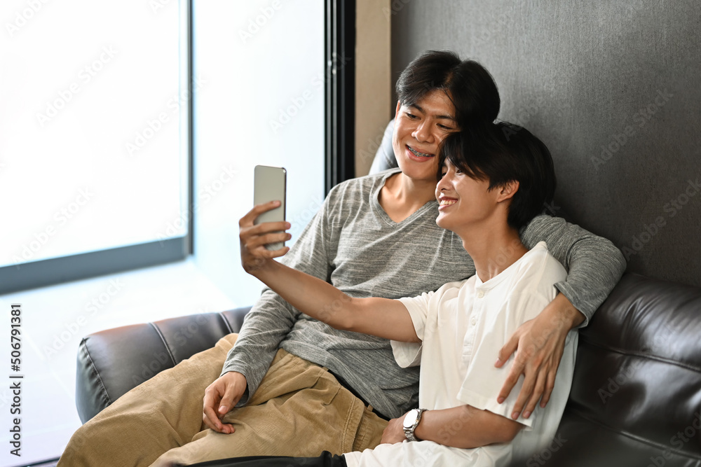 Loving male lgbt couple making selfie while relaxing on sofa at home Loving male lgbt couple making selfie while relaxing on sofa at home