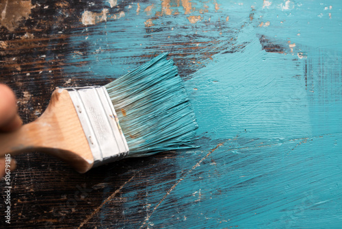 Close up paintbrush in hand and painting on the wooden table.