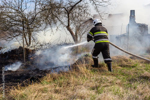 spring fire, burning dry grass near buildings in the countryside. Firefighter extinguishes the flame. Environmental disaster