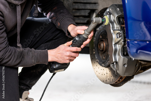Car detailing - Hand with orbital polisher in auto repair shop, polishing modern car brakes