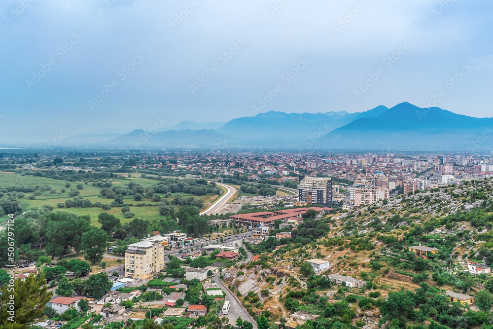 Shkoder, Albania - June 21, 2021: Top view of the highway to Shkoder and the city on the horizon against the backdrop of mountains, Albania. Beautiful Albanian urban-natural panorama on a summer day