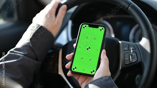 Closeup shot of smartphone with mockup green screen held by the female driver in car over the steering wheel photo