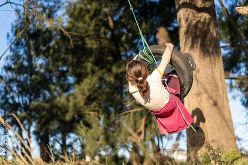 Foto Young girl on tire swing in the backyard swinging back and forth having fun