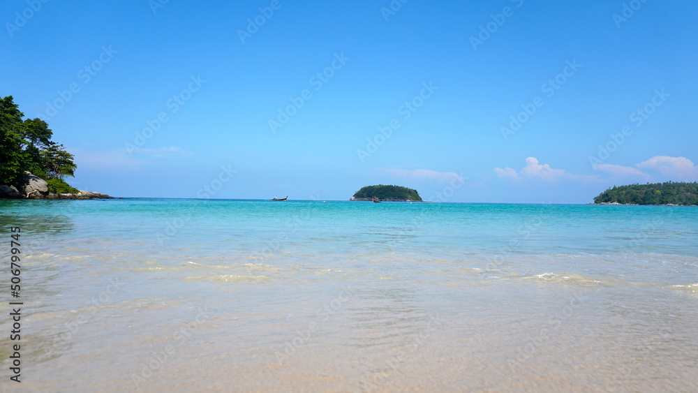 A lonely island in the sea. A Thai fishing boat floats nearby. Clear blue water, snow-white sand. Small clouds in the sea. Palm trees and trees grow on the island. Beautiful Kata beach, Phuket A lonely island in the sea. A Thai fishing boat floats nearby. Clear blue water, snow-white sand. Small clouds in the sea. Palm trees and trees grow on the island. Beautiful Kata beach, Phuket