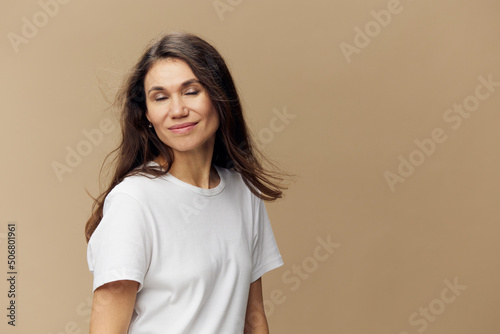 a beautiful, happy woman standing on a beige background with long hair developing in the wind, standing with her eyes closed. Horizontal studio photo
