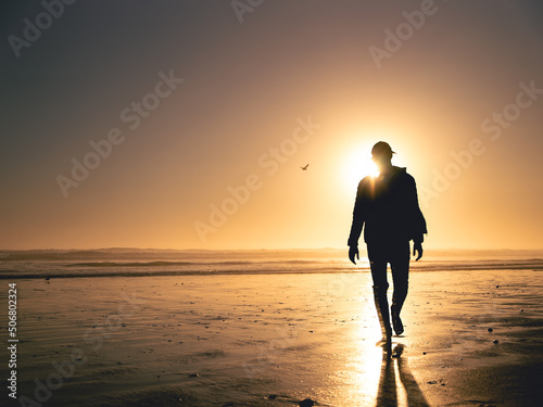 Silhouette of a man walking away from the sun on the beach
