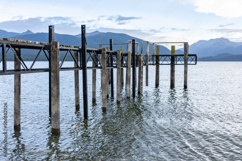 Pier projecting into lake Te Anau from low perspective with mountain range background.in scenic New Zealand image. Pier projecting into lake Te Anau from low perspective with mountain range background.in scenic New Zealand image.