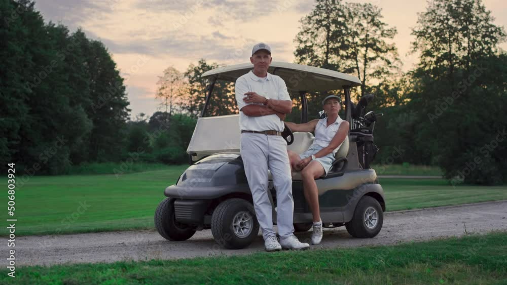 Couple posing golf cart outside. Two golfers take clubs sport equipment on field