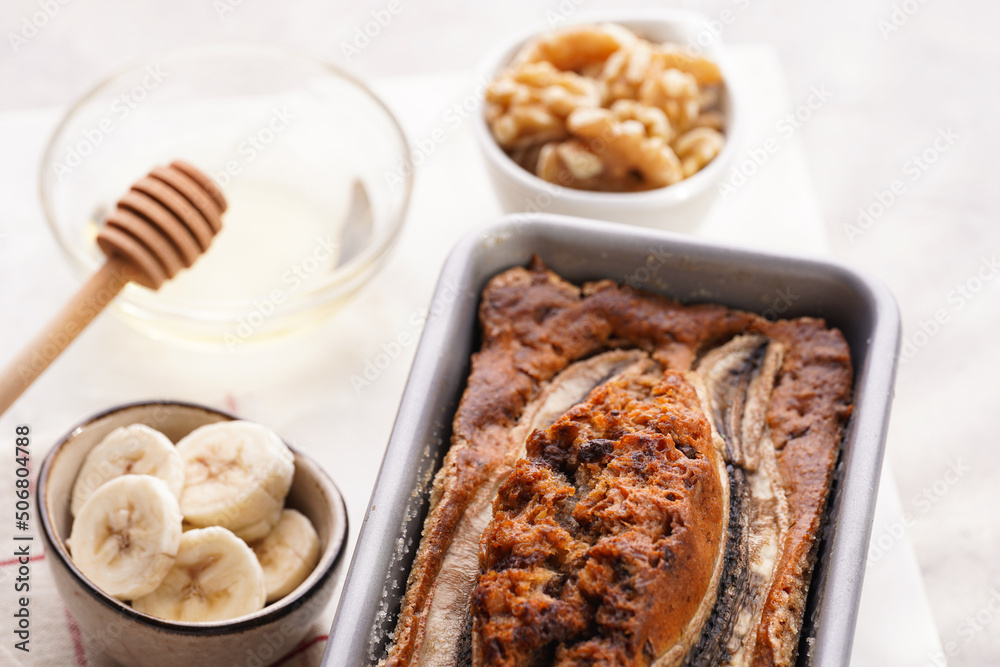 Chocolate banana bread with walnuts in a metallic baking mold and ingredients on a grey neutral background with creative lighting, top view Chocolate banana bread with walnuts in a metallic baking mold and ingredients on a grey neutral background with creative lighting, top view