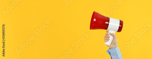 Female hand with megaphone on yellow background