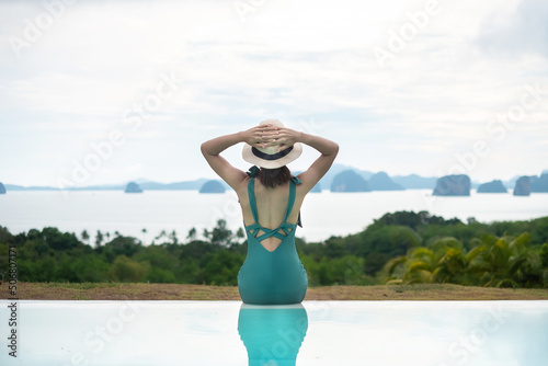 Happy woman in green swimsuit swimming in luxury pool hotel against ocean nature background, young female with hat enjoy in tropical resort. Relaxing, summer travel, holiday, vacation concept © Jo Panuwat D