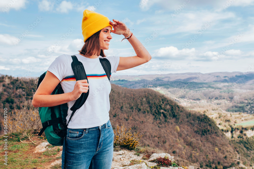Young happy smiling woman, wears yellow beanie and backpack, hiking in the mountains. Top view, landscape, adventure concept. Young happy smiling woman, wears yellow beanie and backpack, hiking in the mountains. Top view, landscape, adventure concept.