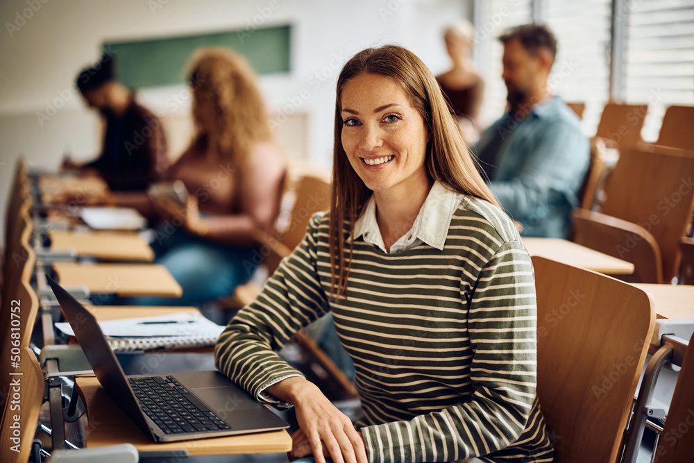 Happy mid adult woman using laptop during class at lecture hall and looking at camera. Happy mid adult woman using laptop during class at lecture hall and looking at camera.