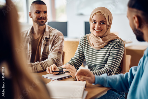 Happy Muslim student talks to her classmates while learning together at college classroom.