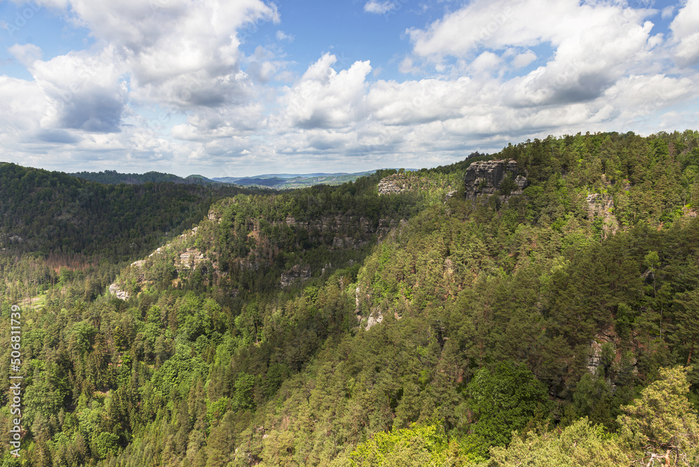 Beautiful view of the landscape of Bohemian Switzerland. The photo shows rocks between trees and clouds in an otherwise blue sky. The photo is taken from the top of Maria Rock.