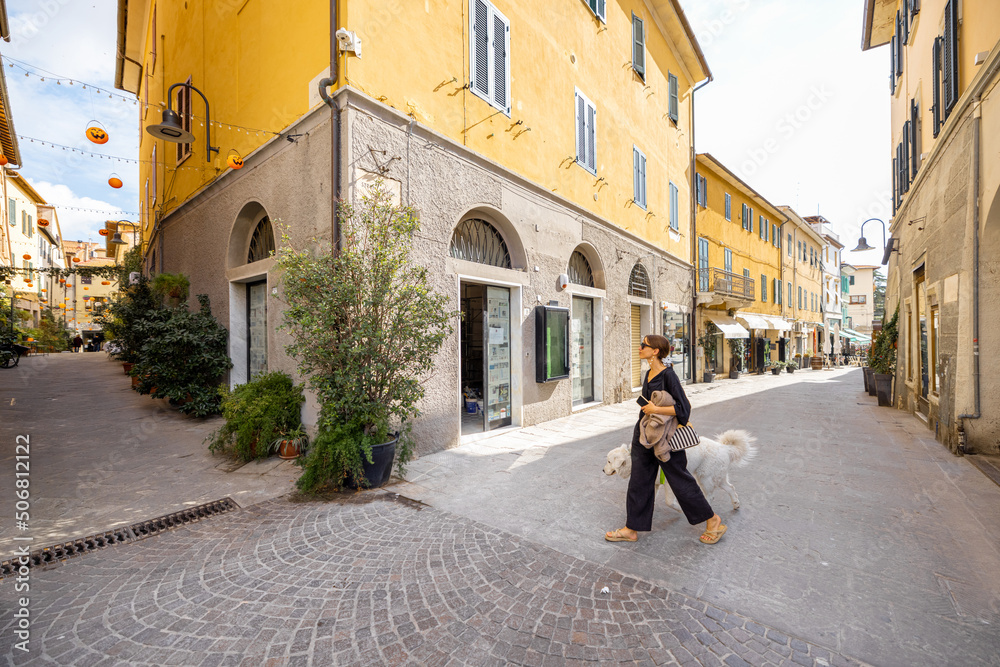 Woman walking with dog on narrow street in the old town of Grosseto, in Maremma region of Italy. Cozy city view of the old Italian town