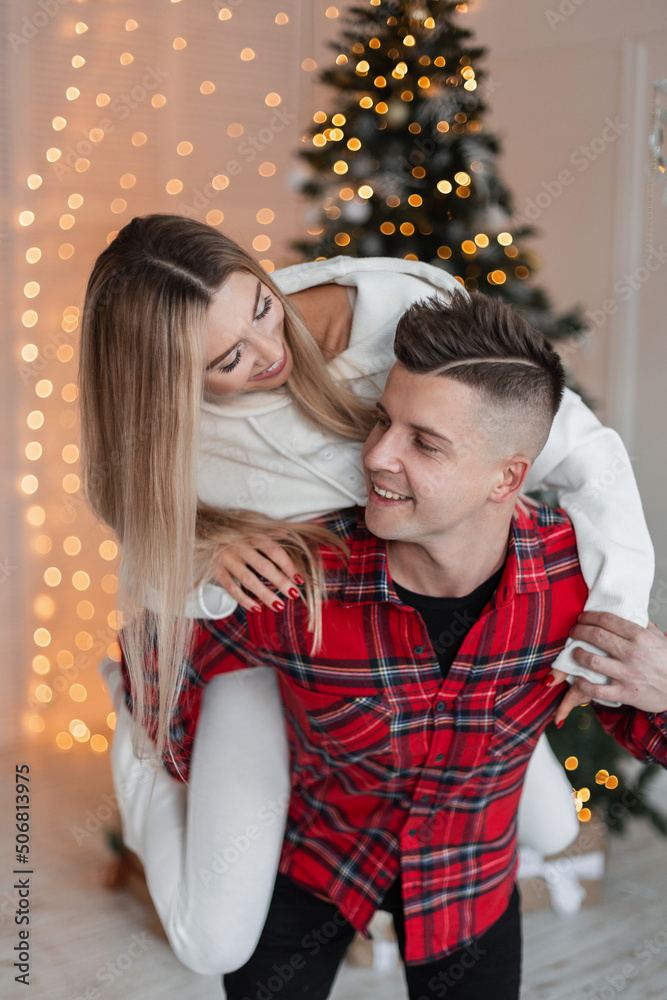 Beautiful young fun-loving couple in fashion clothes are having fun and having fun in front of a Christmas tree and lights Beautiful young fun-loving couple in fashion clothes are having fun and having fun in front of a Christmas tree and lights