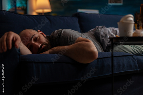 Depressed anxious adult with mental illness laying on couch, feeling pensive and frustrated. Sad desperate man with suicidal thoughts resting on sofa, dealing with chronic disease difficulties.