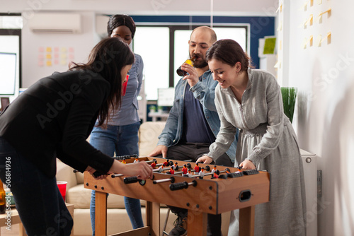 Office workmates playing foosball table game together after hours, enjoying alcoholic drinks and pizza. Man and women doing party celebration and having fun with match after work. photo