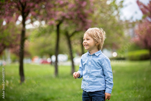 Blond toddler child, cute boy in casual clothing, playing with soap bubbles in the park