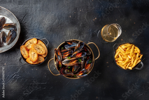 Cooked mussels with French fries and toasted bread, with a glass of white wine, top shot on a black slate background with copy space
