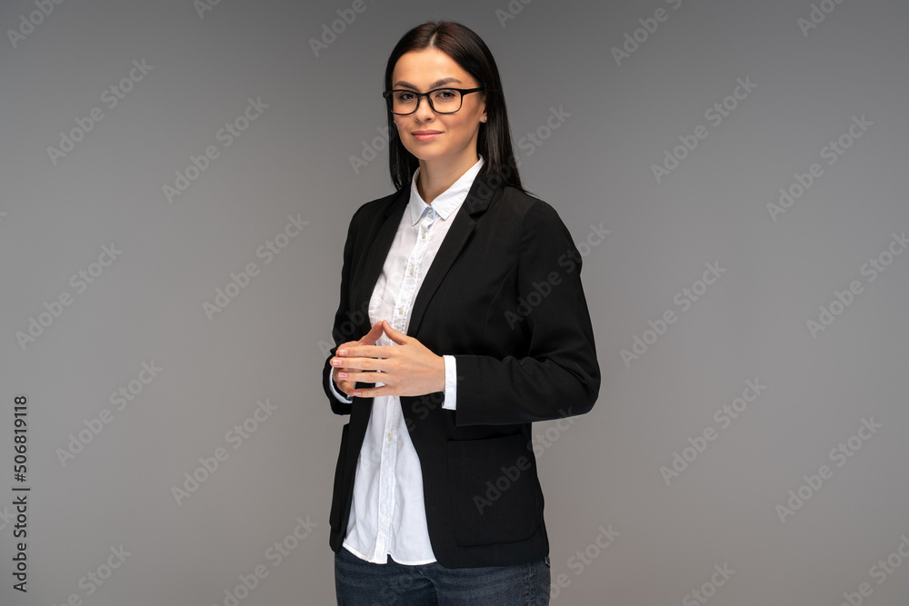 Portrait of cheerful businesswoman wearing glasses smiling at camera, having positive mood. Indoor studio shot, isolated on grey background
