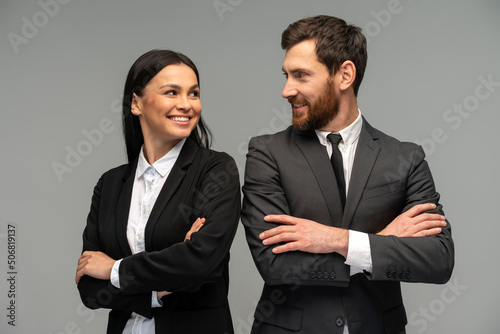Confident happy young business partners looking at each other while posing isolated on grey background. Business concept