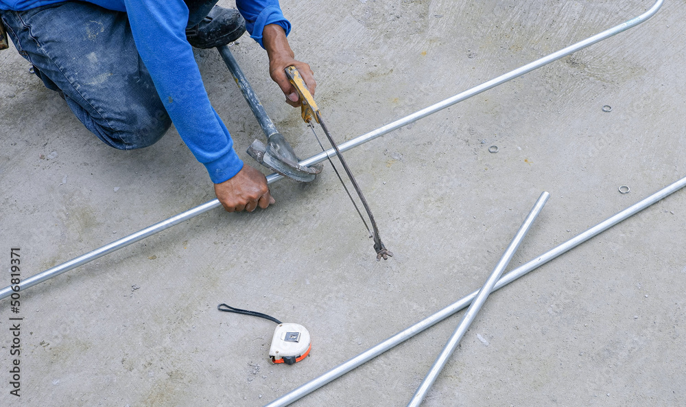 Builder worker using hacksaw to cutting conduit pipes on concrete floor