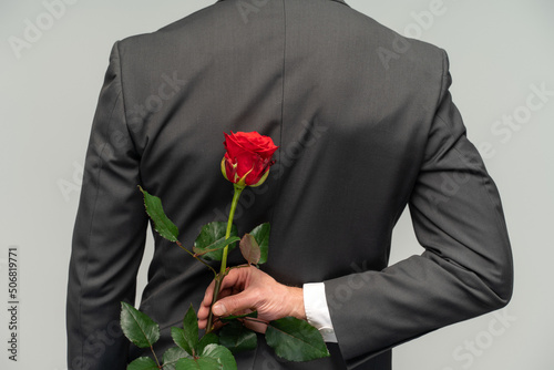 Happy valentines day. Handsome man hide rose behind back while prepare surprise for romantic date. Black suit for formal events