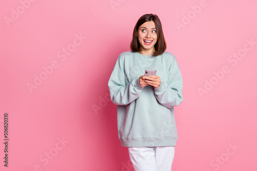 Photo of young cheerful lady hold mobile curious look empty space app download isolated over pink color background
