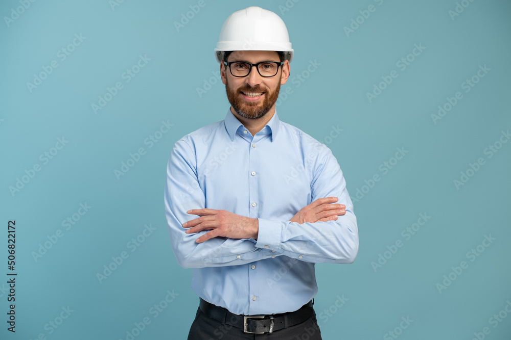 Young architect man with happy face in builder safety helmet smiling while looking at the camera and posing arms crossed over isolated background Young architect man with happy face in builder safety helmet smiling while looking at the camera and posing arms crossed over isolated background