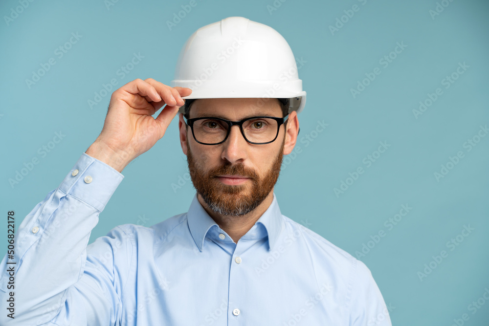 Architect man with serious face in builder safety helmet looking at the camera through his glasses over isolated background. Engineer concept Architect man with serious face in builder safety helmet looking at the camera through his glasses over isolated background. Engineer concept