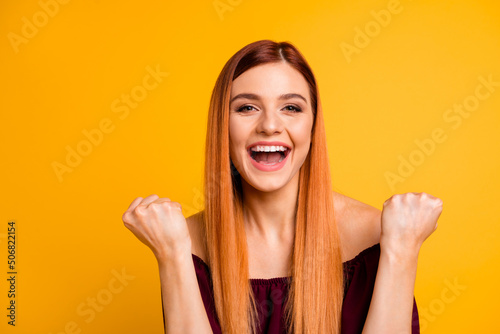 Photo of charming lucky woman wear red outfit smiling rising fists empty space isolated yellow color background