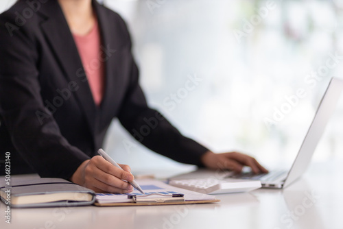 Businesswoman finance market analyst working on laptop pointing at business finance report chart document on desk in office. Financial planning and accounting concepts.