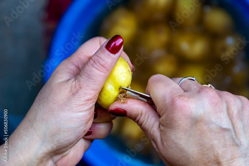 Women s hands peel young potatoes with a special knife  home cooking
