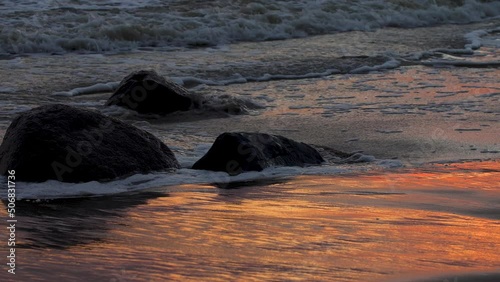 Sea stone of a sandy sea shore after a wave that has just flooded back. Soppy sand turned orange from the light of the sunset. 