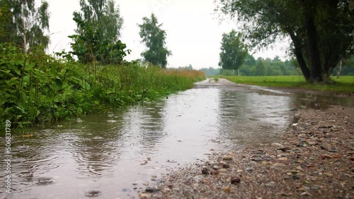 Rural landscape view on raining day. Close up raining over gravel road with puddles on day time.