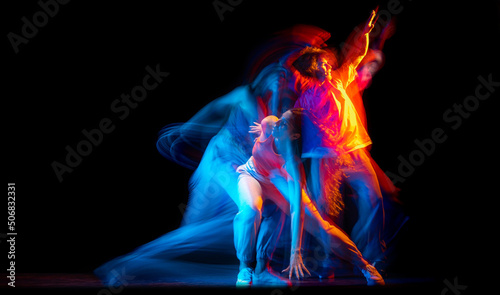 Young man and woman dancing hip-hop in sportive style clothes on dark background at dance hall in mixed neon light. Youth culture, hip-hop, movement