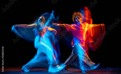 Dance show. Flexible man and girl, hip-hop dancers in motion and action isolated on dark background at dance hall in blue mixed neon light. Youth culture, hip-hop, movement © master1305