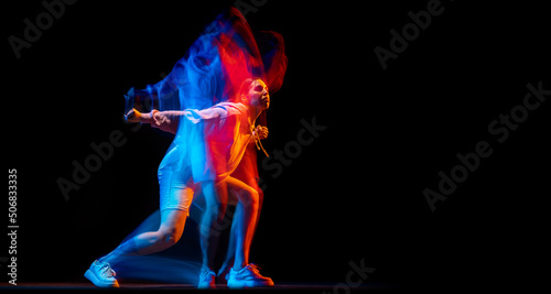 Young woman dancing hip-hop in sportive style clothes isolated on dark background at dance hall in mixed neon light. Youth culture, hip-hop, movement