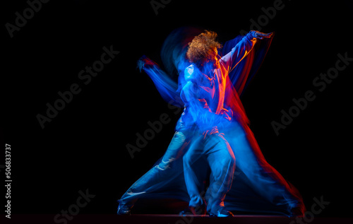 Stylish man dancing hip-hop in sportive style clothes isolated on dark background at dance hall in mixed neon light. Youth culture, hip-hop, movement © master1305
