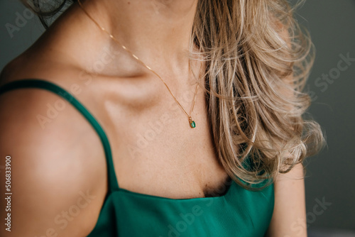Closeup of a blonde woman wearing a golden necklace with an emerald pendant.